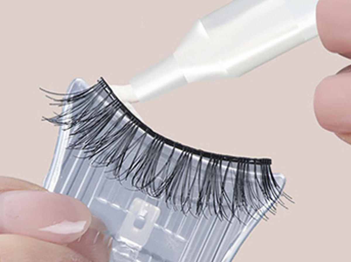 Close-up of a person applying DUO Quick-Set Adhesive to a strip lash using the precision applicator.